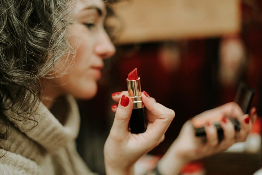 A person in a gray sweater holding a lipstick