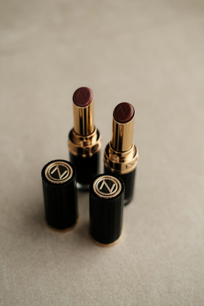 Two dark red lipsticks with gold accents on a neutral surface