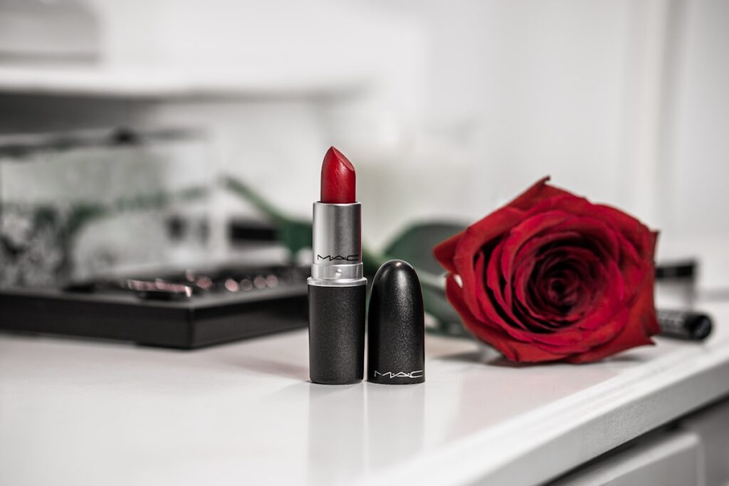 A red lipstick beside a single red rose on a wooden table