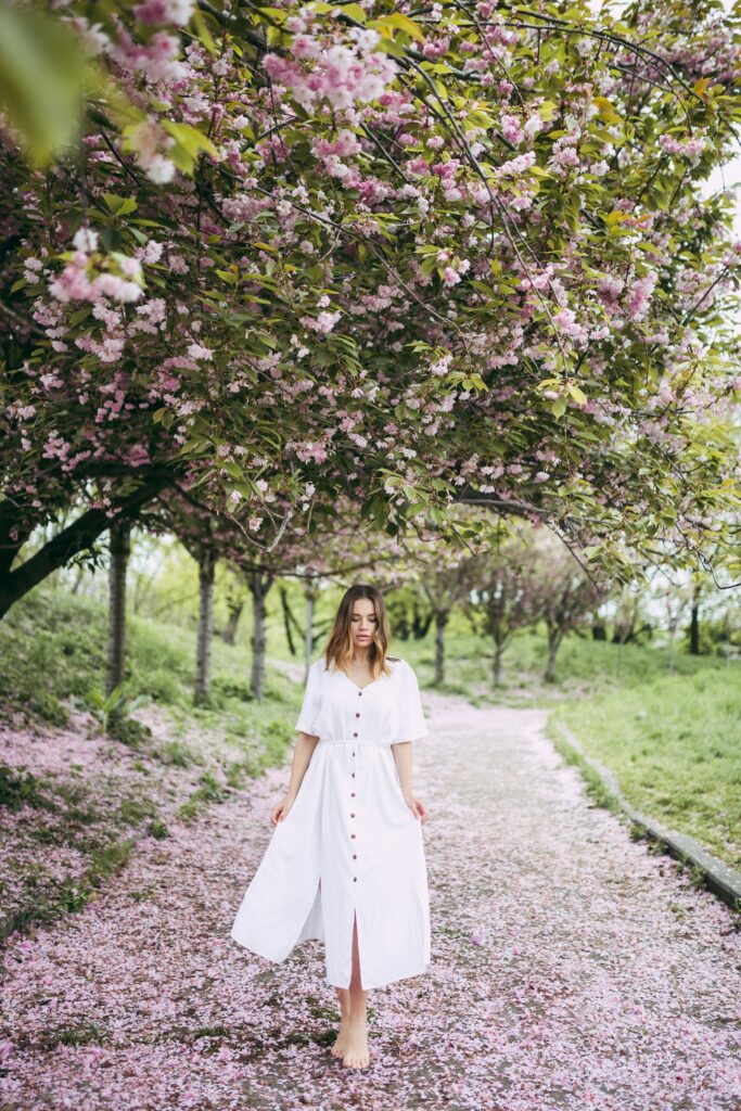 Woman in white dress standing on a trail under a cherry blossom tree