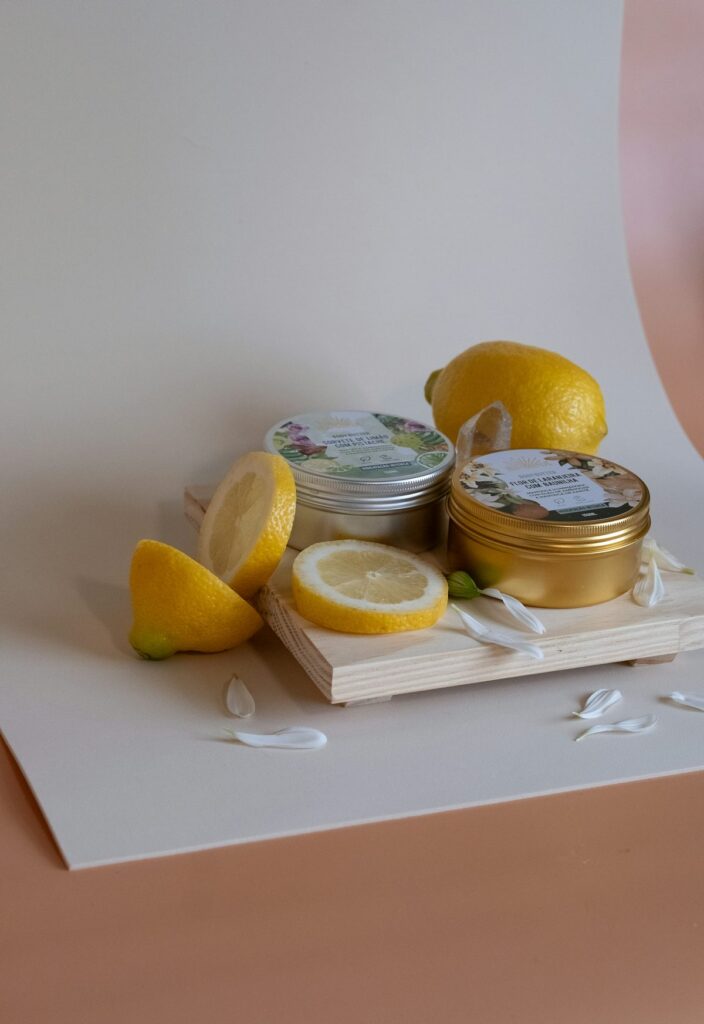 Two small tins, fresh lemons and flower petals arranged on a wooden board