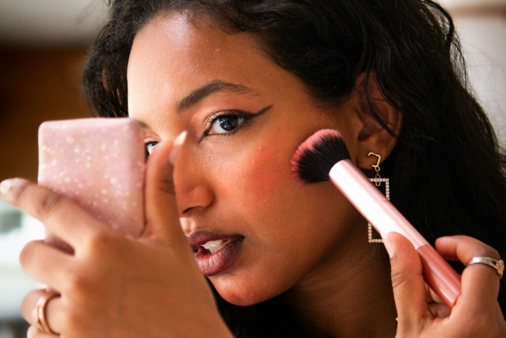 Woman applying blush to softly flushed, glowing cheeks for the cloud skin makeup look