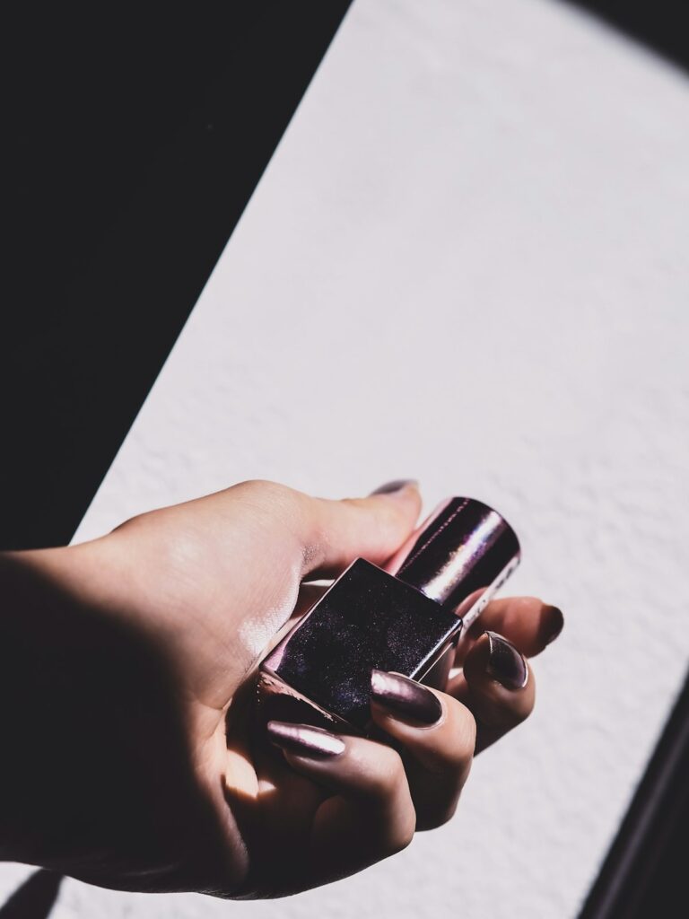 A hand holding a small iridescent fragrance mist bottle in warm sunlight