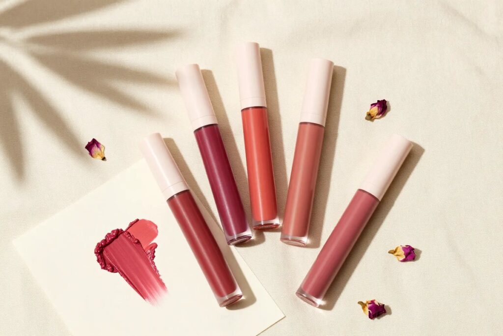 Five unbranded lip tint tubes and lip color swatches on cream linen in summer sunlight