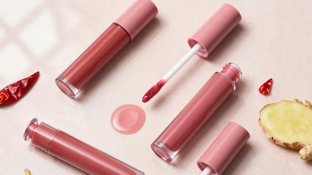 Rosy pink lip plumping glosses on a blush marble surface with chili pepper and ginger